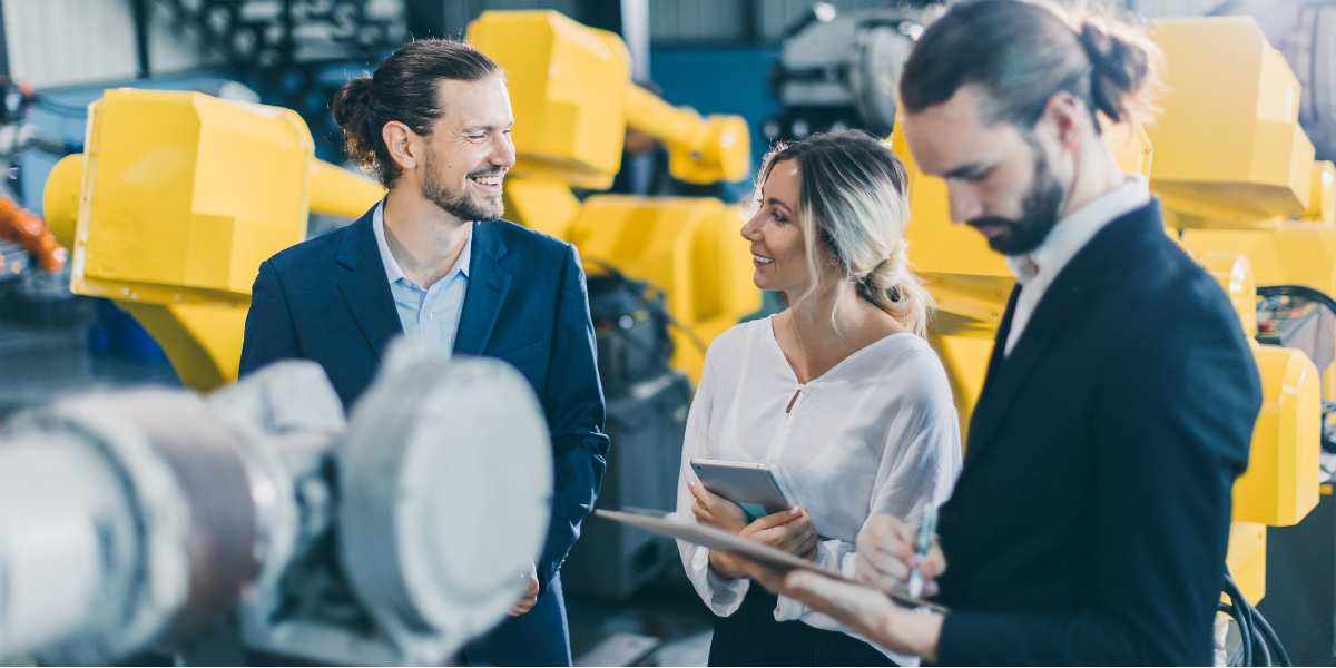 A professional woman with blonde hair meets with two professional men in a manufacturing plant