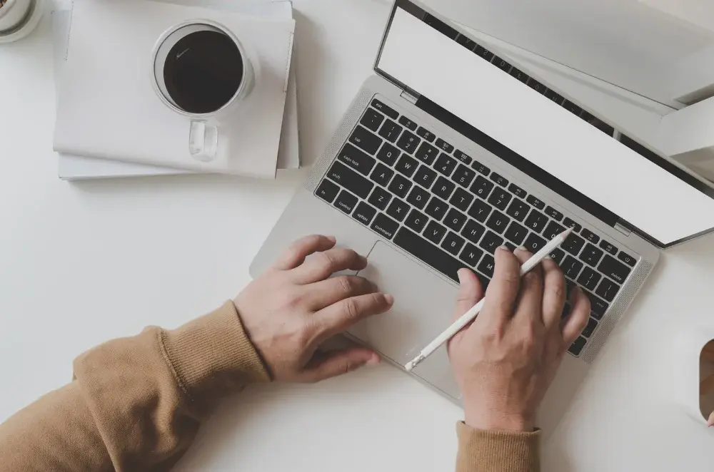 Person working on a laptop at a desk with coffee.